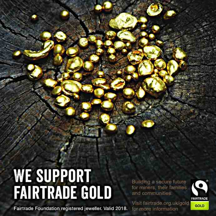 Bright 18ct yellow gold casting grain is scattered across a slice of tree trunk.  The tree drunk is dark and aged with the rings inside showing clearly.  White words say "We Support Fairtrade Gold".  A Fairtrade Gold logo is seen in the bottom right corner.