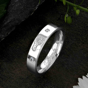 A White Gold Wedding Ring with an engraved baby footprint on the outer surface | Set with two diamonds that frame the footprint | Engraved with the name Elijah on the inside of the ring | Hand engraving | Ladies slim 4mm wide, comfort flat-court profile ring | Custom personalised wedding jewellery | Sophia Alexander Fingerprint Jewellery | Handmade in Suffolk UK