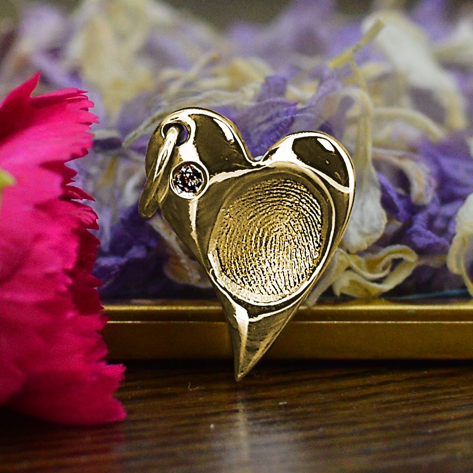 A solid gold heart-shaped necklace featuring a real fingerprint and with cremation ashes set behind a single diamond.