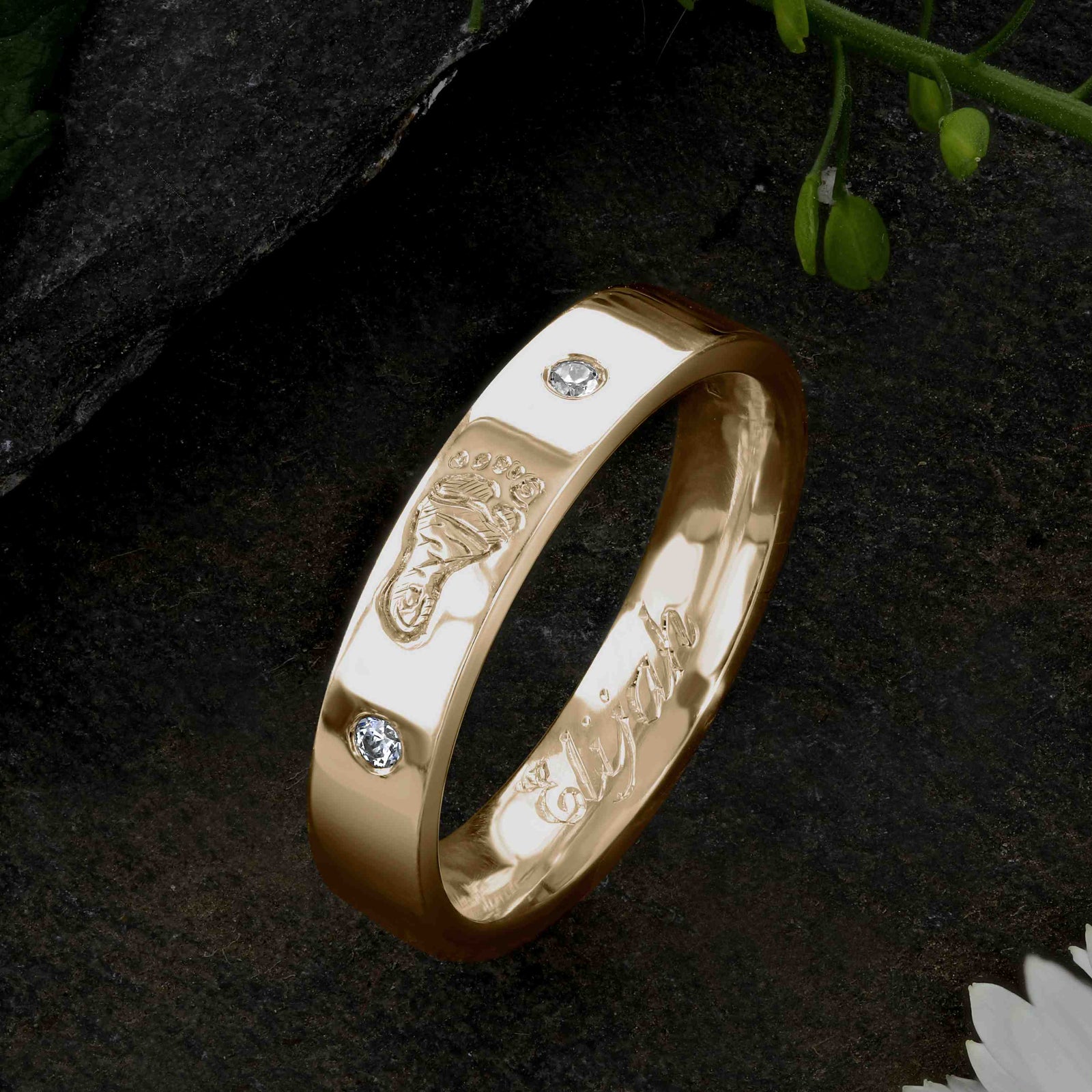 A Gold Wedding Ring with an engraved baby footprint on the outer surface | Set with two diamonds that frame the footprint | Engraved with the name Elijah on the inside of the ring | Hand engraving | Ladies slim 4mm wide, comfort flat-court profile ring | Custom personalised wedding jewellery | Sophia Alexander Fingerprint Jewellery | Handmade in Suffolk UK