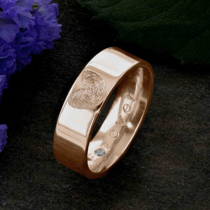 A Rose Gold Wedding Ring with two fingerprints engraved in the shape of a heart on the outer surface | Engraved with the word Forever on the inside of the ring | Set with a single diamond in the O of Forever | Hand engraving | Men's 6mm wide, comfort flat-court profile ring | Custom personalised wedding jewellery | Sophia Alexander Fingerprint Jewellery | Handmade in Suffolk UK